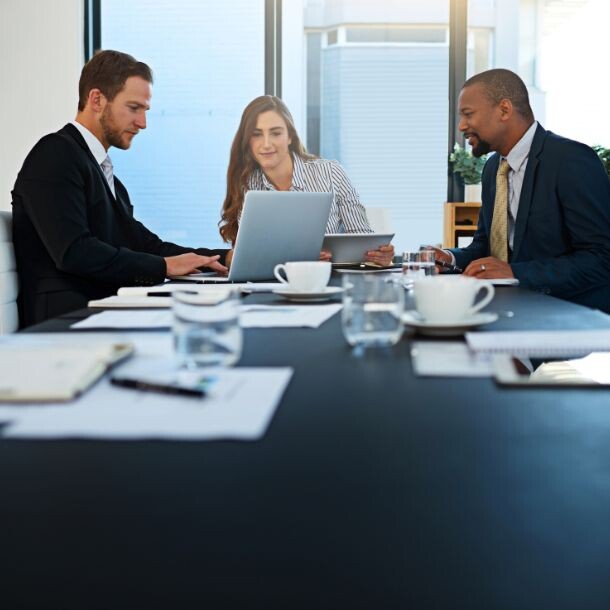 3 people sitting at a conference table looking at a computer