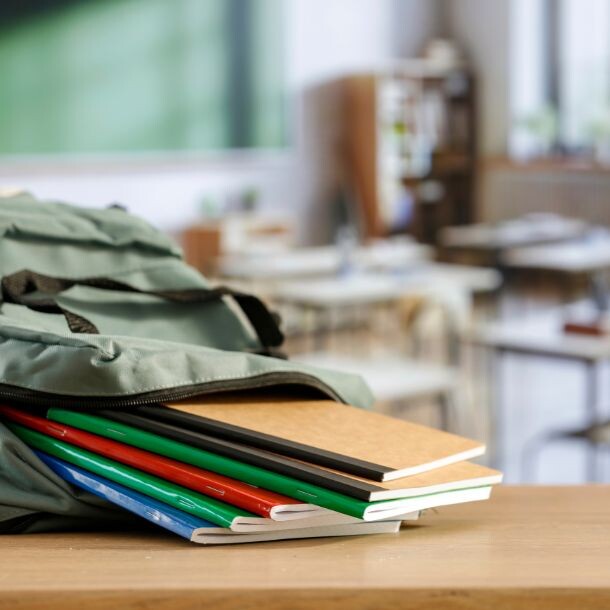 Pile of notebooks falling out of a backpack that is laid on a desk in a classroom.