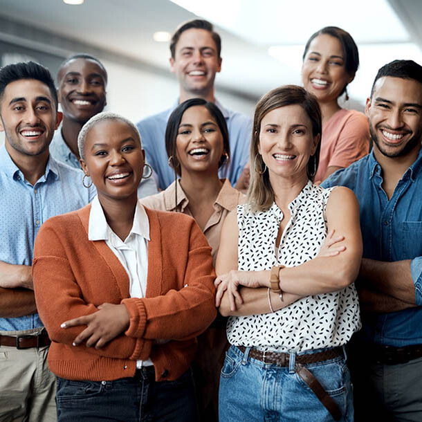 Diverse group of employees at an office, all smiling, crossing their arms and looking at the camera.