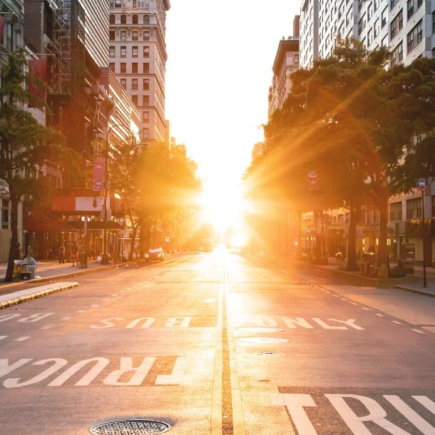 The sun shines almost horizonally into a seemignly calm street right in between two tall buildings, adding a warm tone to the picture.