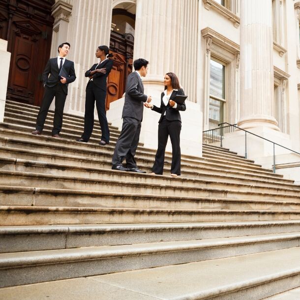 A wideshot of the stairs in front of an official building, with a few people dressed professionally standing and talking to one another.