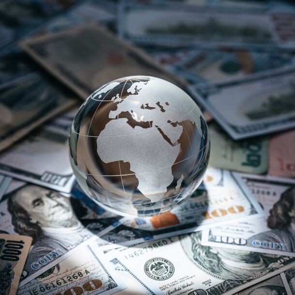A desk scattered with dollar bills, and sitting in the middle is a glass sphere with a solid representation of the countries.