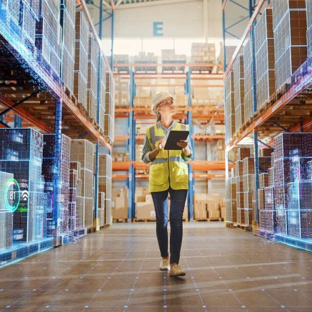 Employee in safety wear walking throuhg a hallway in a warehouse. The shelves are covered with white icons and graphs.