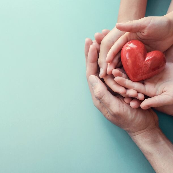 Three pairs of hands (one pair is a child's) holding a heart.