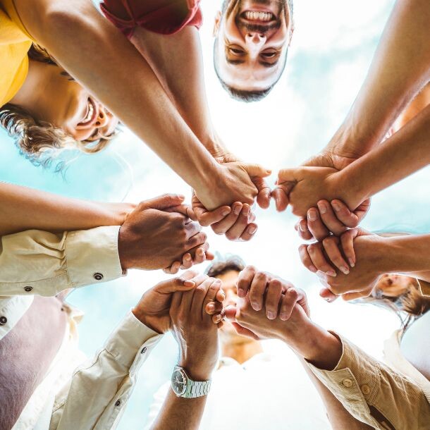Shot from the ground up, a group of people holding each other's hands in the middle of a circle.