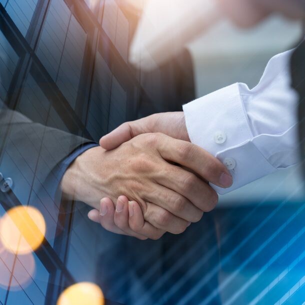 A handshake overlayed at the sides by glass buildings.