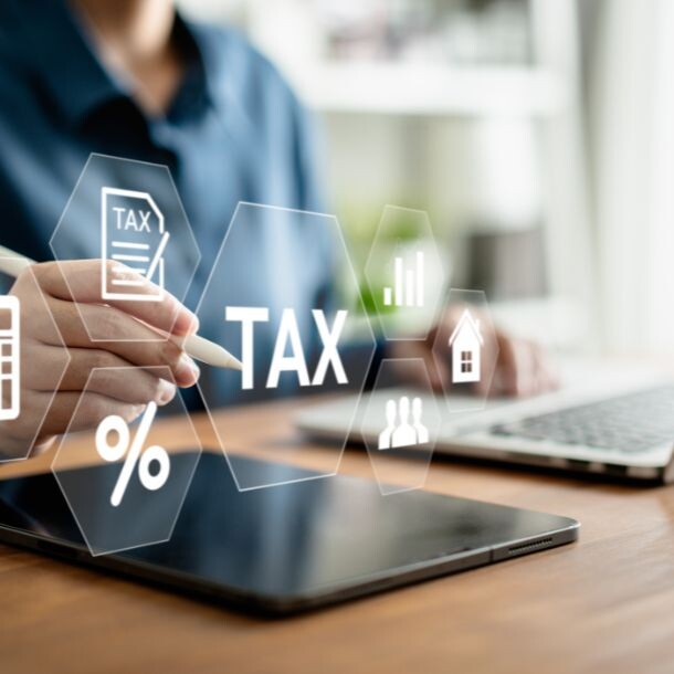A person typing on a laptop keyboard while icons float on top of it. Some of the icons represent percentages, TAX, a calculator, and a group of people.