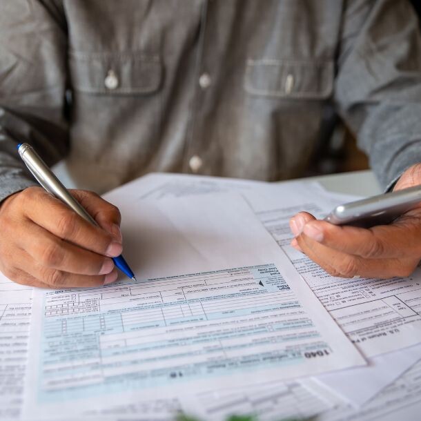 A person holding their phone with their left hand and writing on a report with their right hand.