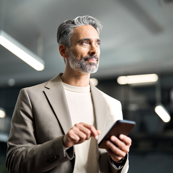 Business professional in office holding a smartphone and looking ahead