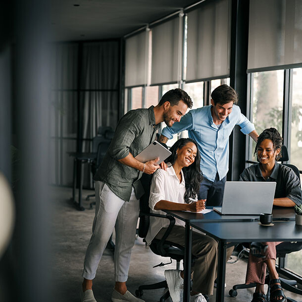 Team of coworkers gathered around a laptop collaborating at a table