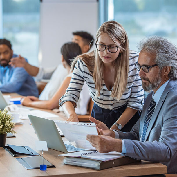 Two coworkers reviewing documents together at a desk with a laptop