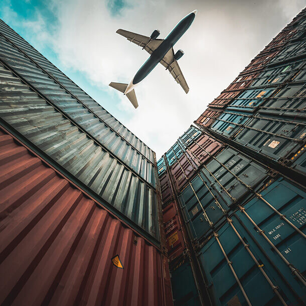 Freight airplane flying above shipping containers representing global logistics.
