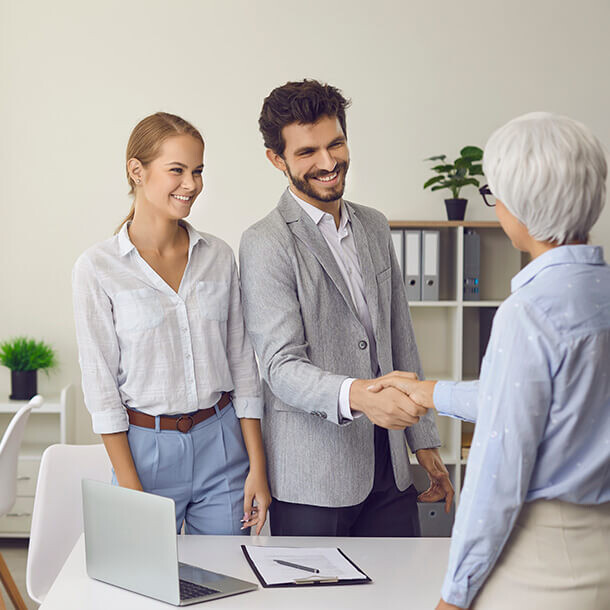 Couple shaking hands with a female financial advisor representing business trust.