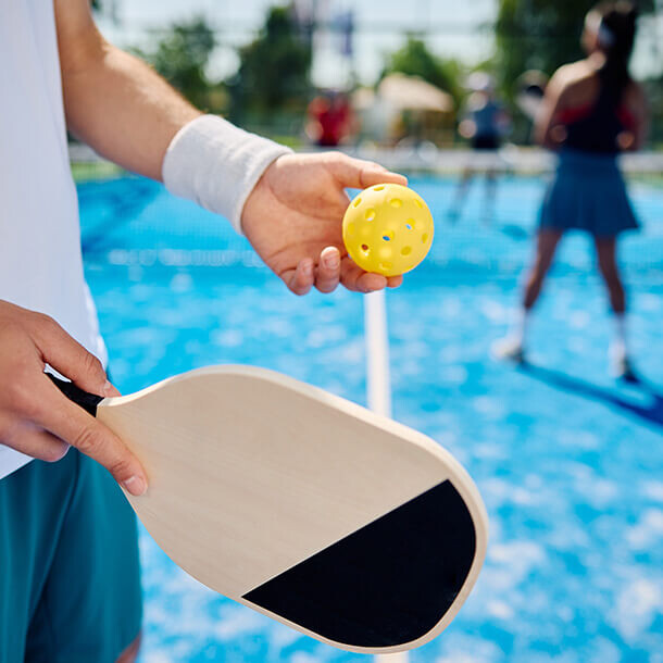 Pickleball player serving the ball on an outdoor court.