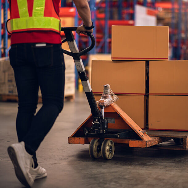 Factory worker using a hand pallet truck to move boxes in a warehouse.