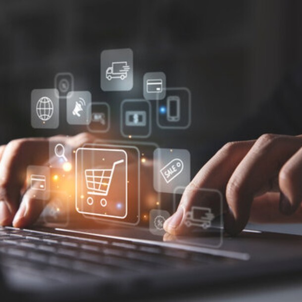 Hands using a laptop with digital shopping cart and e-commerce icons displayed on screen.
